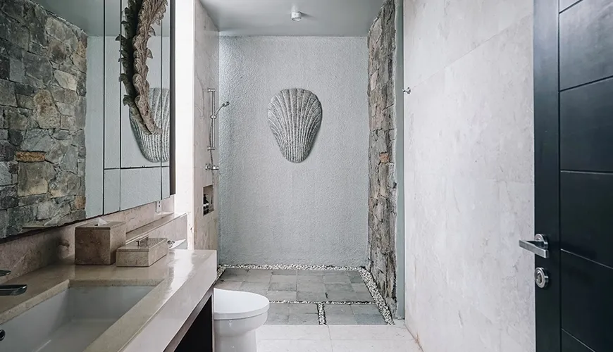 Ambergris Villa, Nusa Dua, Bali — luxurious bathroom with natural stone wall modern shower pebble drainage vanity mirror and seashell artwork | The Luxury Bali