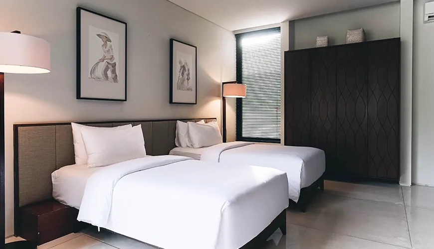Ambergris Villa, Nusa Dua, Bali — modern twin bedroom with two white beds floor lamps traditional framed artwork and dark wood wardrobe | The Luxury Bali