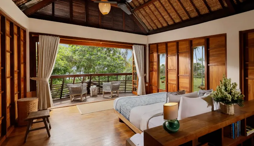 The Cove Bali, Tabanan, Bali — rustic wooden bedroom with thatched roof and balcony overlooking tropical garden | The Luxury Bali