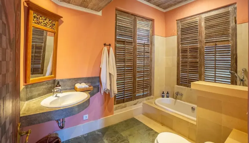 Villa Angsa, Sanur, Bali — bathroom with peach colored walls a mirror wooden shutters and a white bathtub | The Luxury Bali