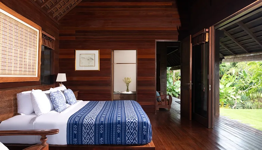 Villa Bangkuang, Canggu, Bali — luxurious wooden villa bedroom featuring a bed with blue patterned linens and garden view access | The Luxury Bali