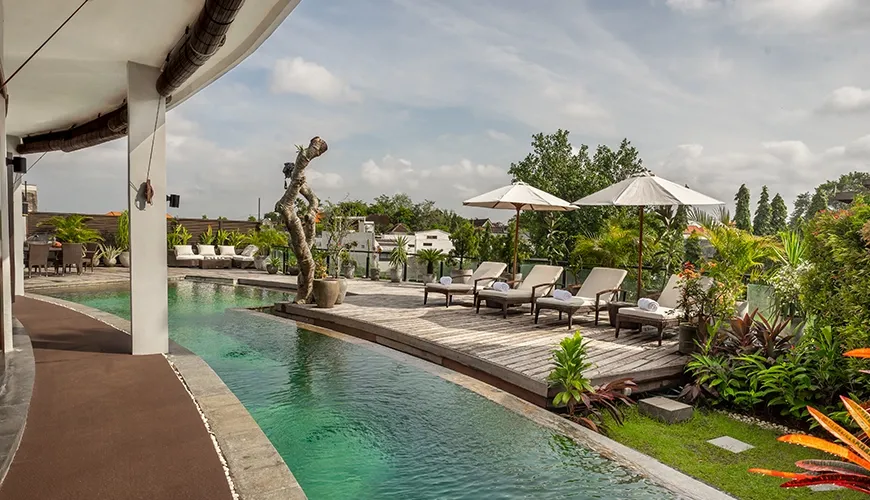 Villa Oshra, Canggu, Bali — curved swimming pool with sun loungers and tropical foliage | The Luxury Bali