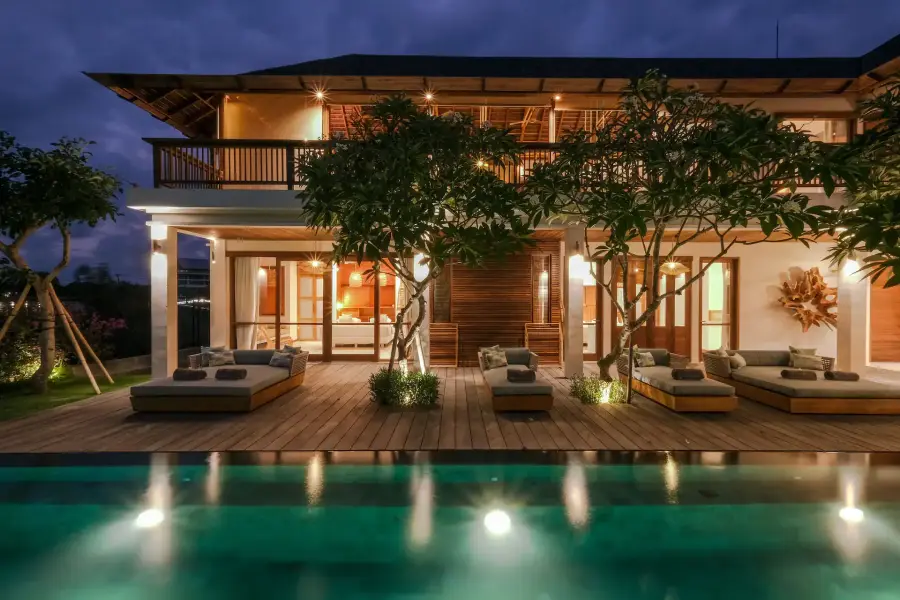 A six-bedroom villa in Uluwatu, Bali: the timber house lit at dusk behind the pool
